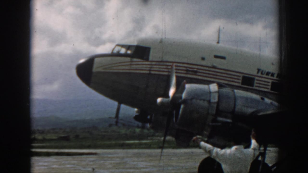 1962 Izmir tarmac view of a Turkish Airlines propeller aircraft, seen close from below with cloudy sky and distant hills.