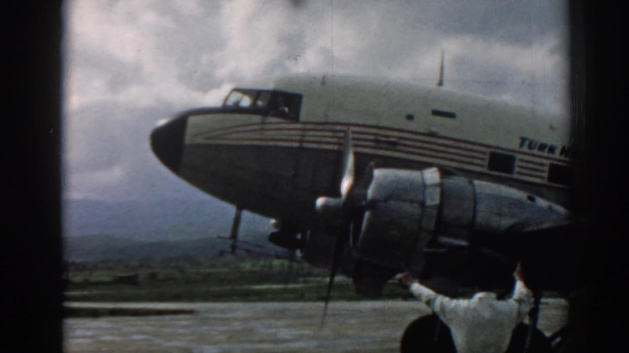 Close tarmac view of a propeller aircraft nose and engine with a person below the wing.