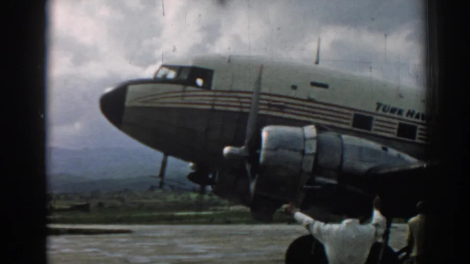 1962 Izmir airport frame showing the aircraft fuselage, propeller engine, and partial figures along the tarmac edge.