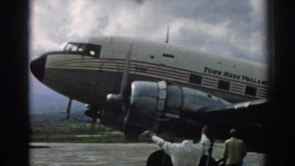 1962 Izmir home-movie frame of a Turk Hava Yolları aircraft nose, engine, and two men below the wing area.