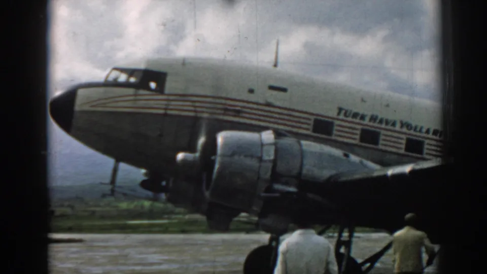 1962 Izmir frame showing the Turk Hava Yolları propeller engine and men near the aircraft under a cloudy sky.