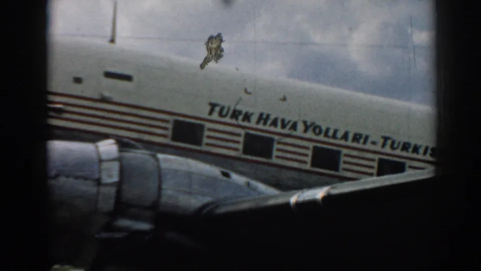Close 1962 Izmir frame of the Turk Hava Yollari fuselage, engine, windows, and wing captured on grainy 8mm film.