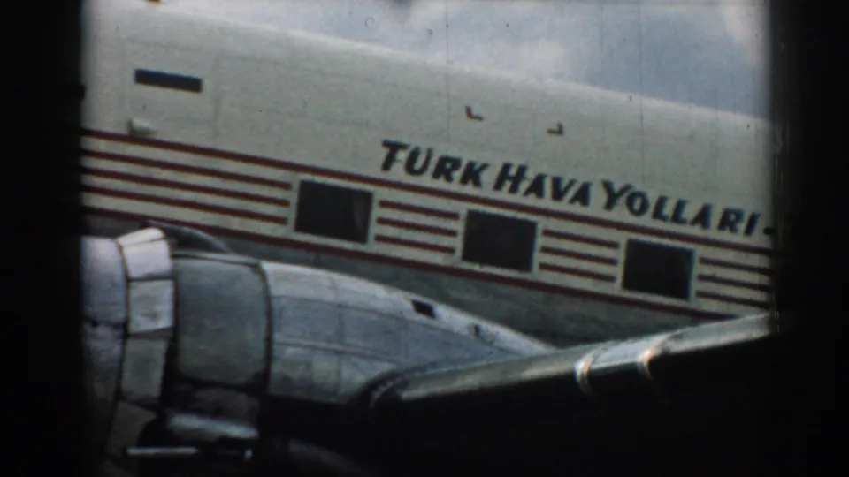 Close 1962 Izmir view of a Turk Hava Yollari plane, with fuselage lettering, windows, red stripes, and wing visible.