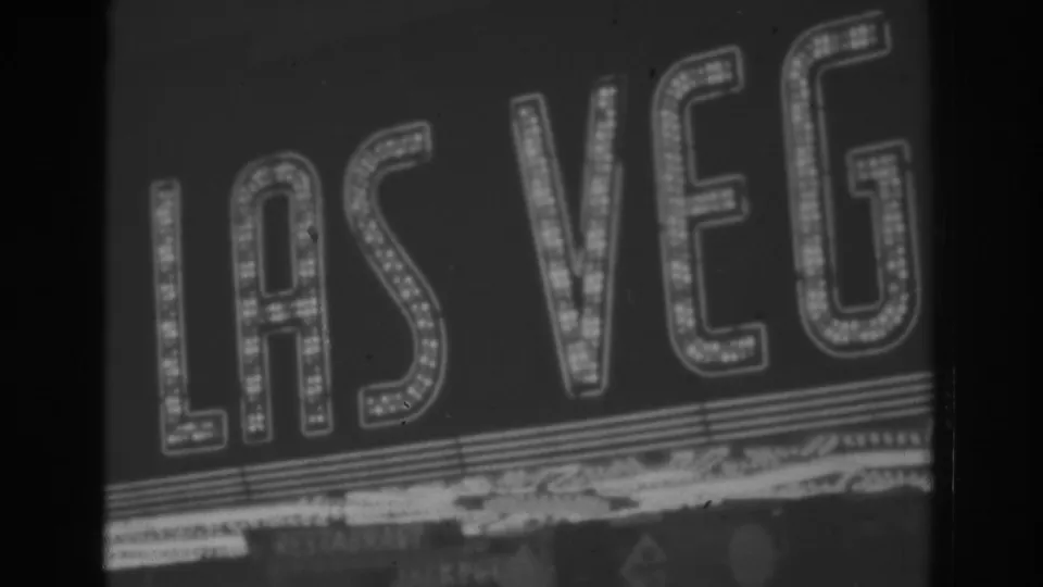 Nighttime 1962 Las Vegas frame showing bright marquee-style LAS VEGAS letters in black-and-white 8mm footage.