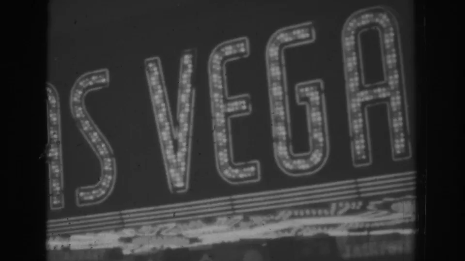 Close-cropped nighttime frame of glowing Las Vegas marquee letters, with grain and scratches visible in the 8mm scan.