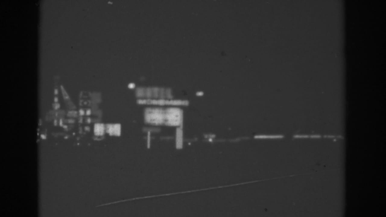 Distant illuminated motel and building signs seen across a dark roadside foreground.