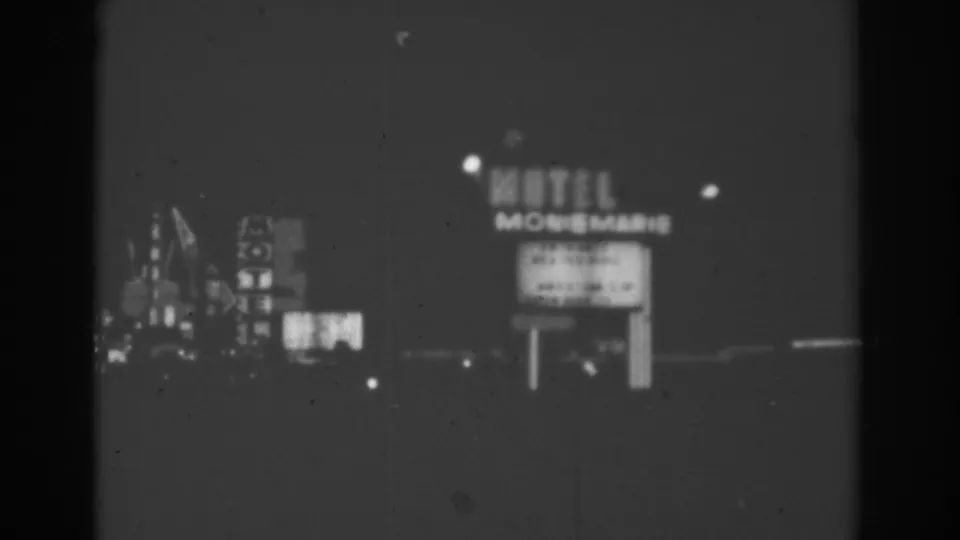 Black-and-white 1962 Las Vegas frame with a Motel Monte Marie roadside sign, nearby illuminated structures, and dark roadway foreground.