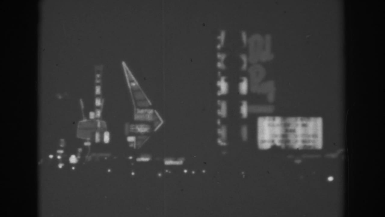 Blurred nighttime roadside signs with tall vertical lettering and arrow-shaped neon.