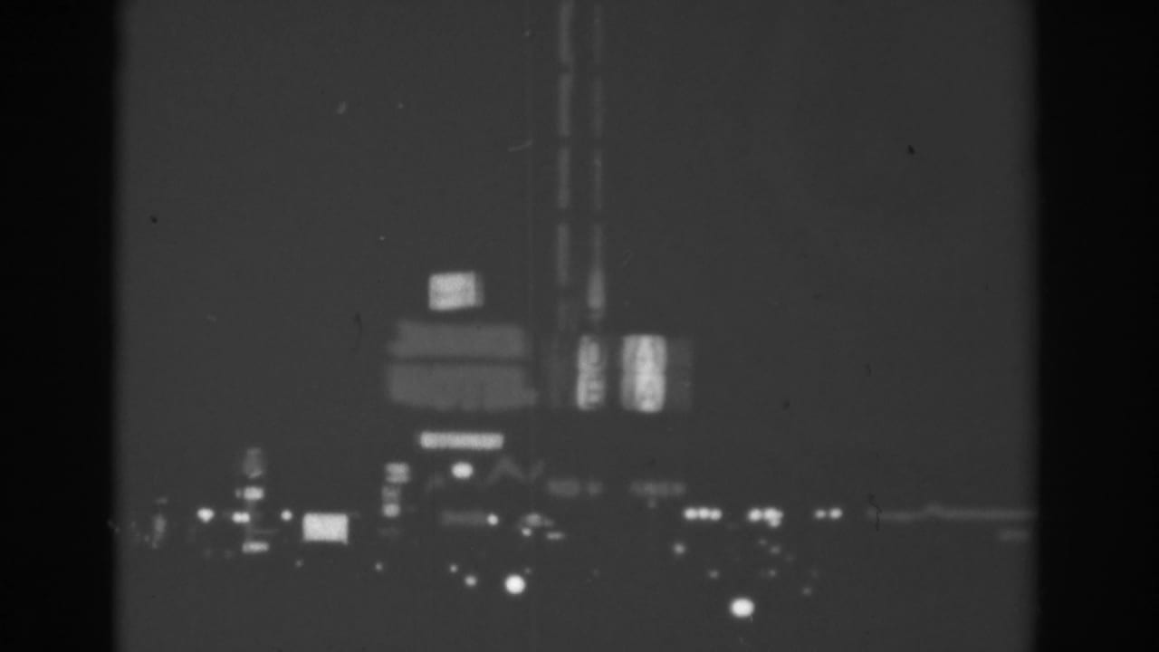 Black-and-white Las Vegas boulevard view with illuminated motel and roadside signs softened by motion and low light.