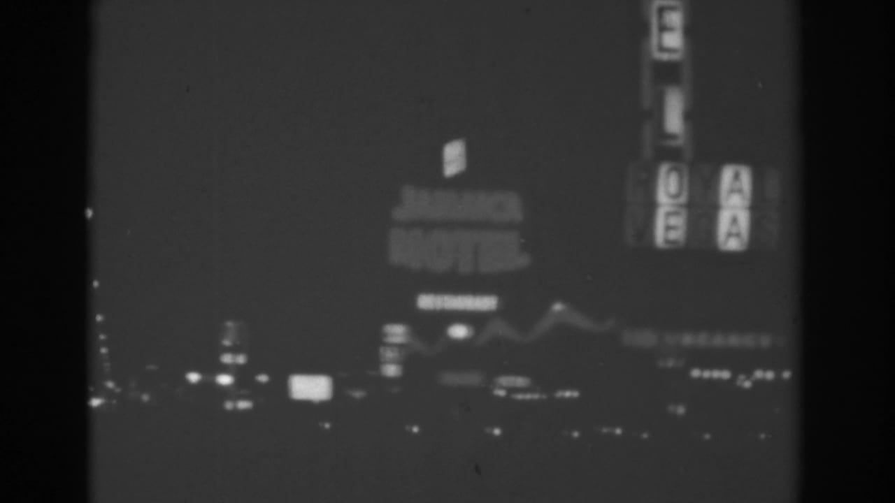 1962 Las Vegas night frame with a lit motel sign, vertical roadside letters, and scattered car lights along the boulevard.