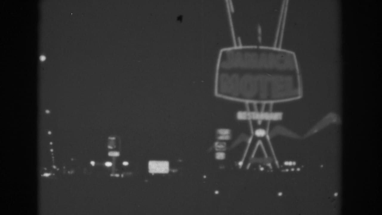 Black-and-white 1962 Las Vegas frame centered on a large retro motel sign, with distant signs and roadway lights below.