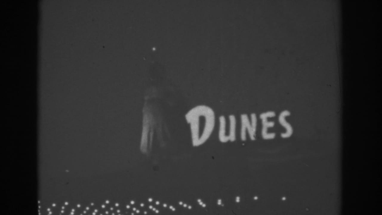 1962 Las Vegas home-movie frame showing the illuminated Dunes sign with rows of small lights beneath it at night.
