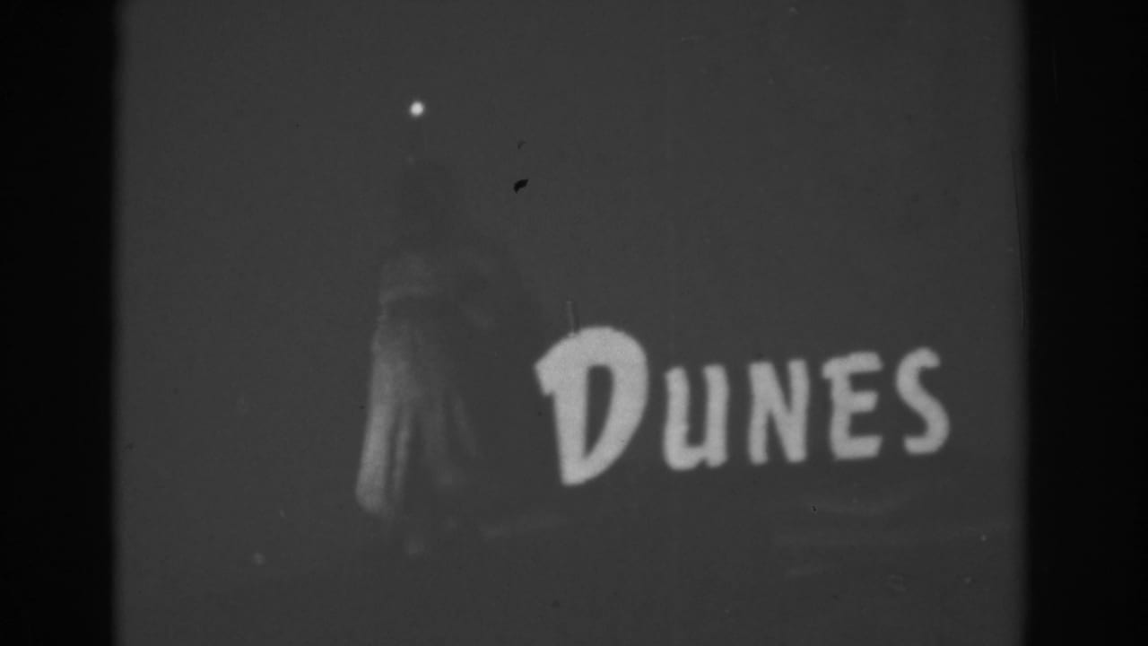 1962 Las Vegas home-movie frame showing the Dunes sign at night, with a faint standing figure or sign element visible at left.