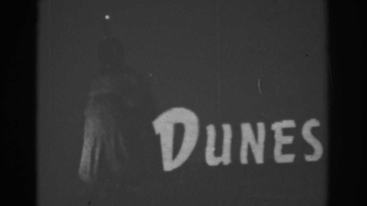 1962 Las Vegas home-movie frame showing a closer view of the Dunes sign, with a dim standing figure or sign element at left.