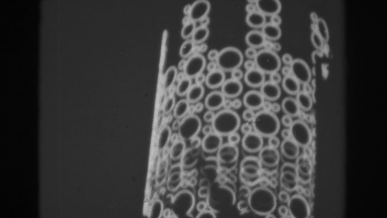 Nighttime Las Vegas frame with a tall sign covered in circular bulbs and animated light forms, seen in soft 8mm focus.