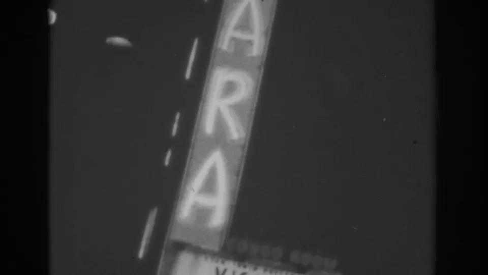 A Las Vegas vertical sign fills the frame at night, with large glowing letters and part of a marquee below.