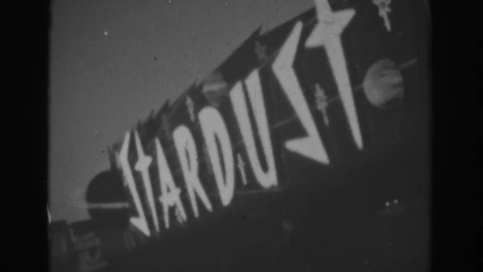 1962 Las Vegas frame of the Stardust sign, with oversized letters and star motifs captured in grainy black-and-white 8mm.