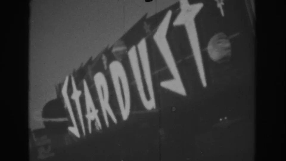 1962 Las Vegas 8mm still showing a closer tilted view of the Stardust sign, with bold white letters and star shapes dominating the frame.