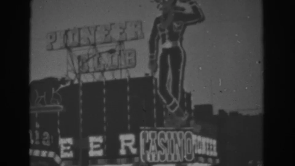 1962 Las Vegas frame showing the Pioneer Club casino sign, including a large female neon figure, block lettering, and casino signage below.