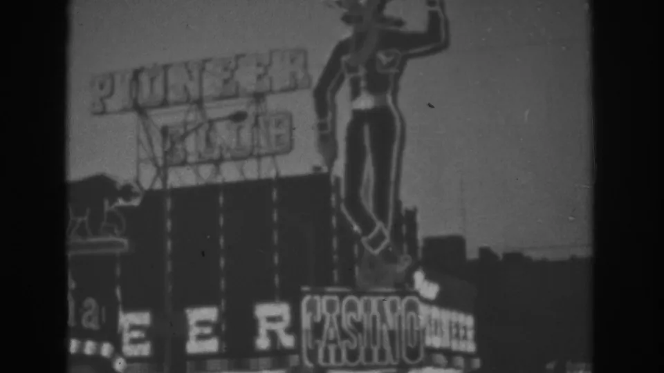 1962 Las Vegas home-movie frame showing soft-focus Pioneer Club signage, casino marquee text, and Western cowboy figure.