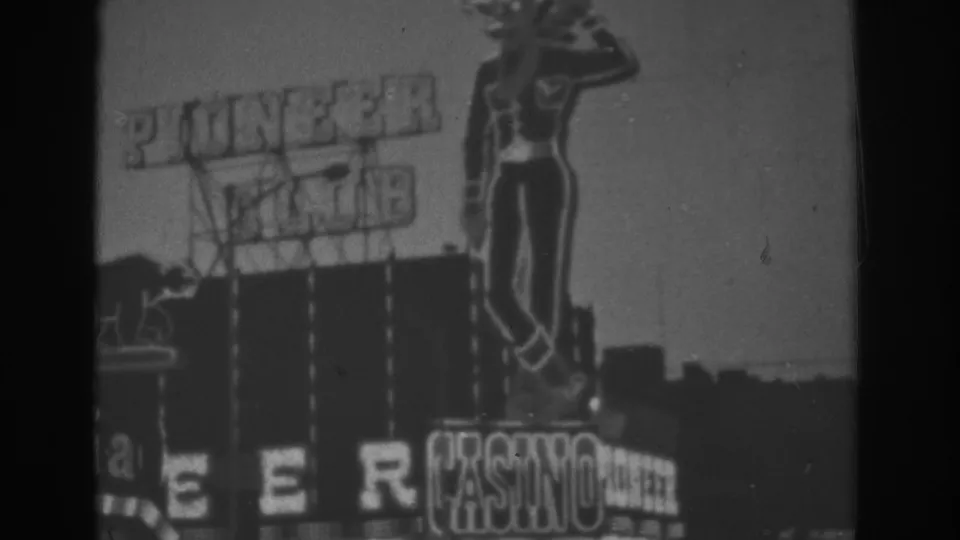 Grainy 1962 Las Vegas 8mm frame of the Pioneer Club casino sign, cowboy figure, roofline, and clear sky.