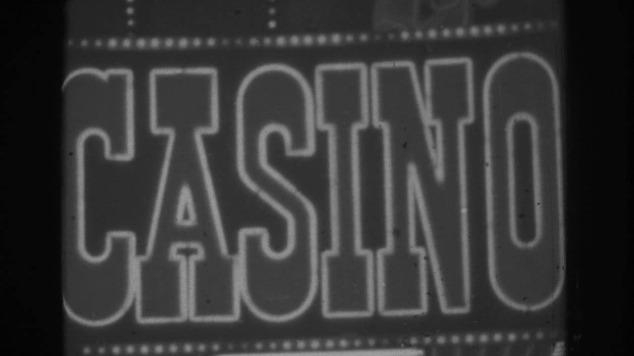 Close black-and-white 8mm frame of a Las Vegas CASINO sign, with illuminated border bulbs and soft evening exposure.