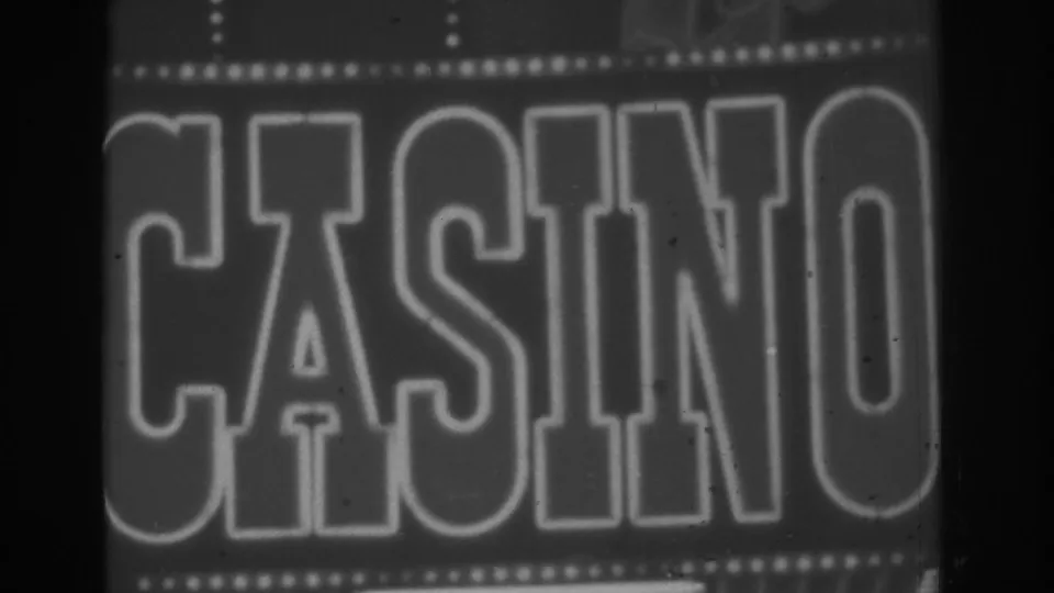 Close black-and-white 8mm frame of a Las Vegas CASINO sign, with illuminated border bulbs and soft evening exposure.