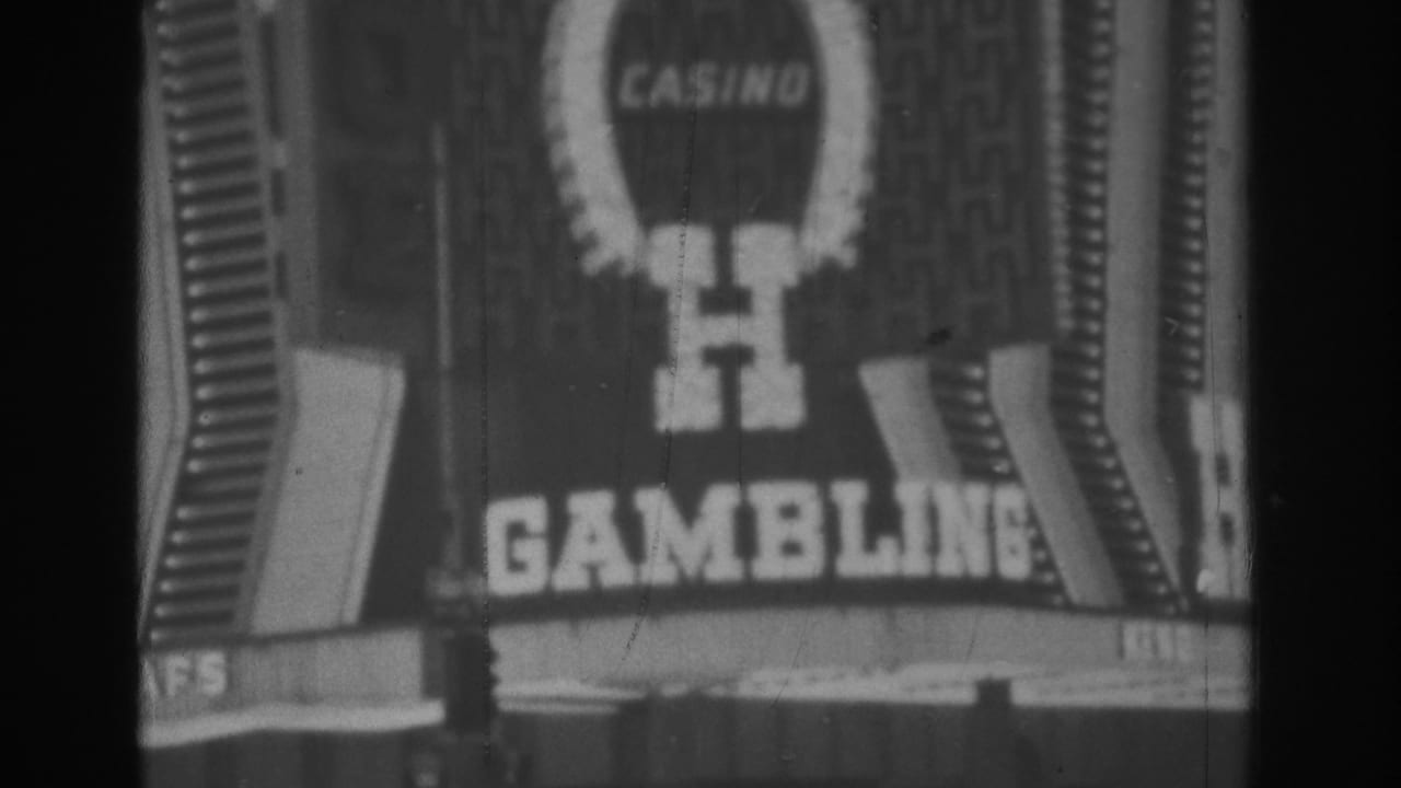 1962 Las Vegas 8mm frame showing an illuminated casino front with a horseshoe logo, casino text, gambling lettering, and cars below.