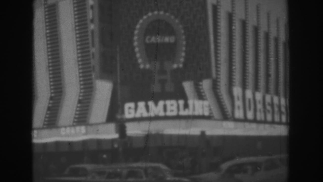 Black-and-white Las Vegas casino exterior with bright horseshoe signage, large gambling text, vertical facade lights, and classic cars along the curb.
