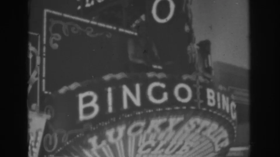 Black-and-white 8mm view of the Lucky Strike Club sign with large BINGO letters and a curved marquee in Las Vegas.