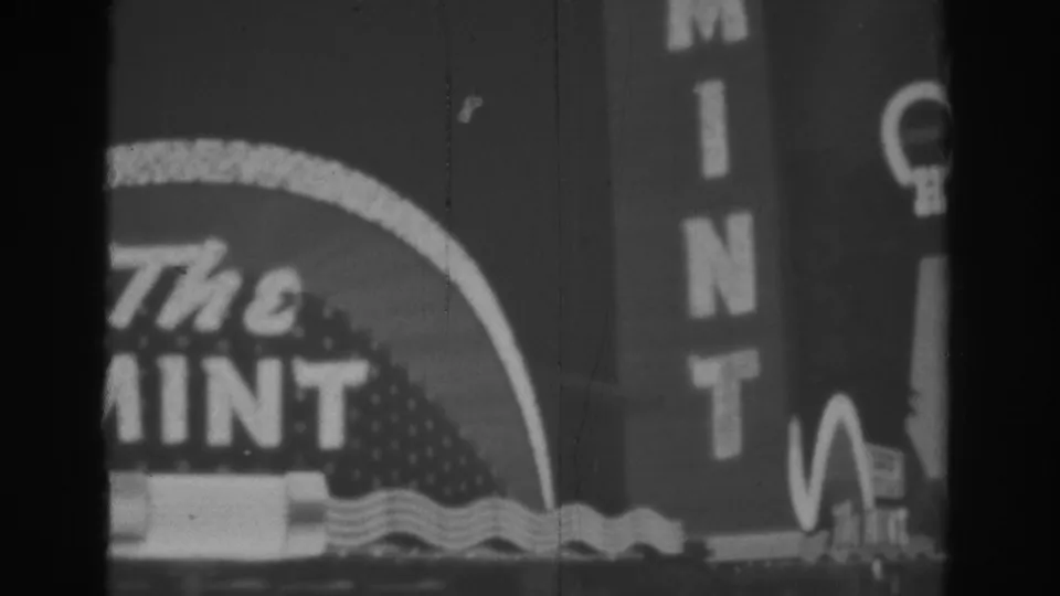 1962 Las Vegas 8mm frame with a cropped view of The Mint sign, vertical MINT letters, and nearby illuminated sign shapes.