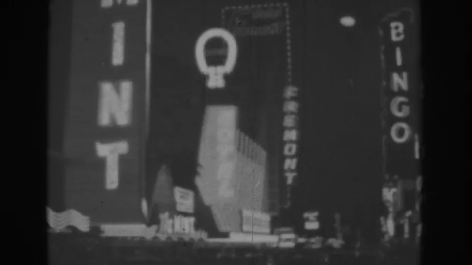 Black-and-white 1962 Las Vegas frame with The Mint sign, a vertical Bingo sign, and neon-lit street frontage.