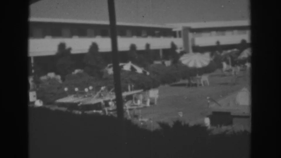 1962 black-and-white resort courtyard view in Las Vegas with shaded umbrellas, lounge furniture, trees, and a modern facade.
