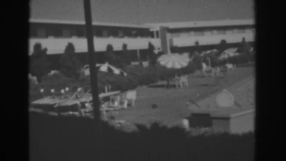 Black-and-white Las Vegas courtyard frame showing a striped umbrella, seating, trees, and a low resort building behind.