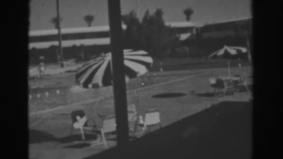 Las Vegas resort pool deck in 1962, showing striped umbrella, lounge chairs, palms, and low hotel buildings.