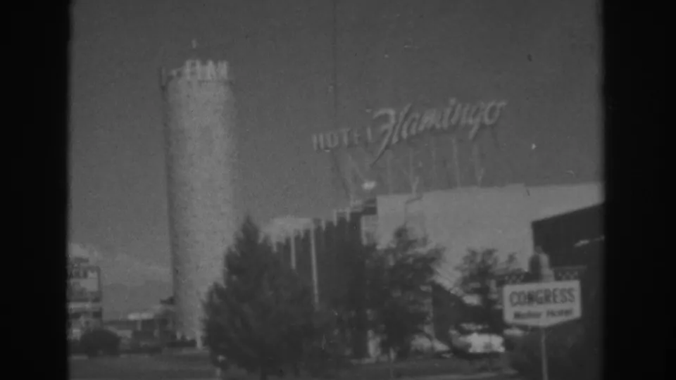 Hotel Flamingo signage in Las Vegas, filmed in 1962 above trees, a cylindrical structure, and roadside signs.