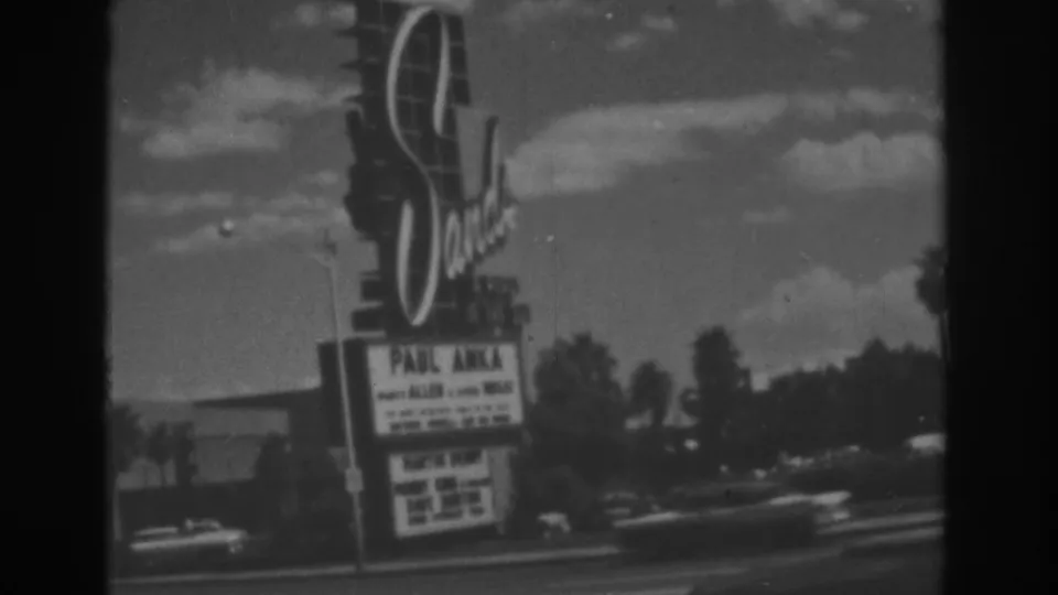1962 Las Vegas frame showing the Sands Hotel sign and marquee advertising Paul Anka beside a palm-lined street.
