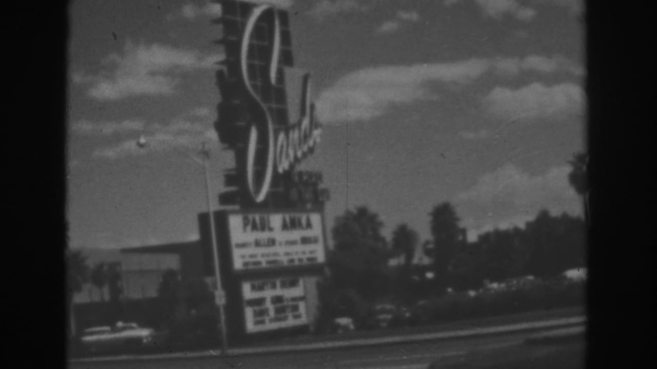 Roadside theater sign and marquee beside a street under a bright sky.