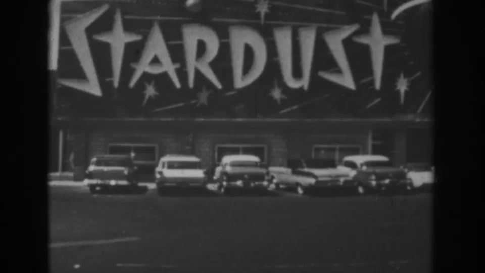 1962 Las Vegas frame showing the Stardust theater facade with large signage above parked mid-century cars.