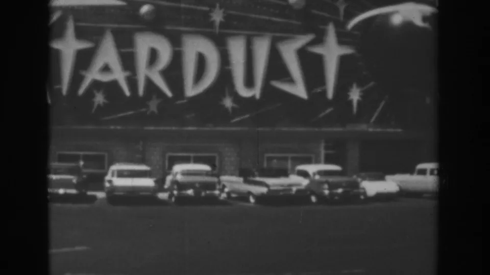 Close 1962 Las Vegas home-movie view of Stardust lettering above sedans and a station wagon in the parking area.