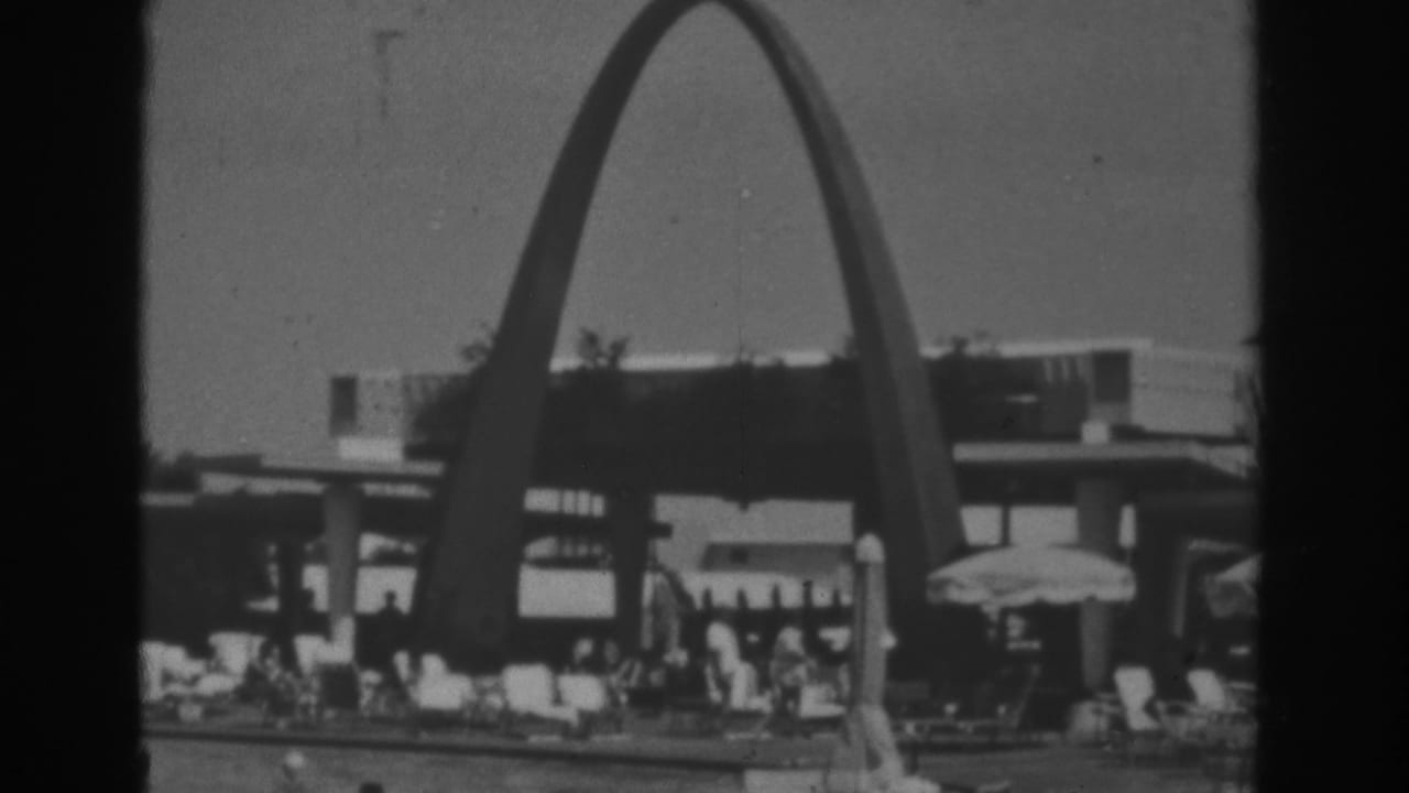 Tall arched resort structure over a poolside area with lounge chairs, umbrellas, and people.