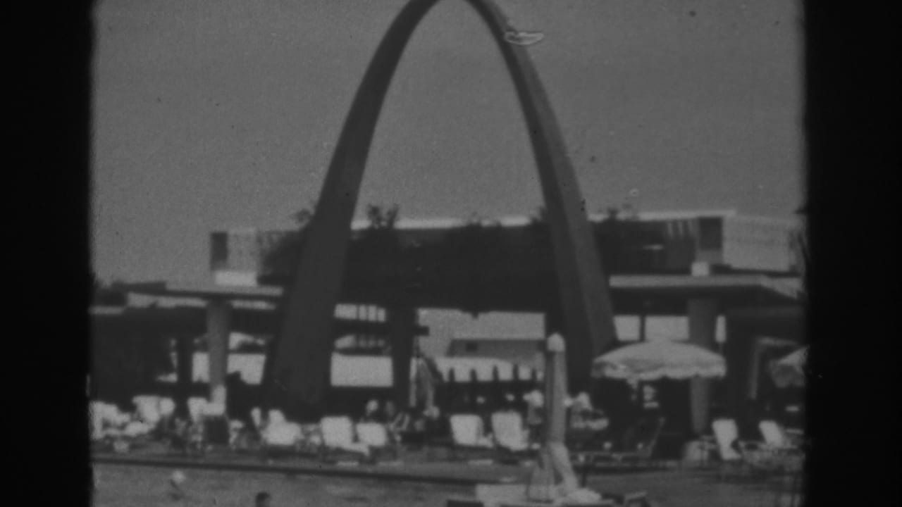 1962 Las Vegas home-movie frame showing the arched resort pool area with lounge chairs, umbrellas, and visitors in soft black-and-white focus.
