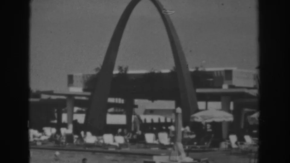1962 Las Vegas home-movie frame showing the arched resort pool area with lounge chairs, umbrellas, and visitors in soft black-and-white focus.