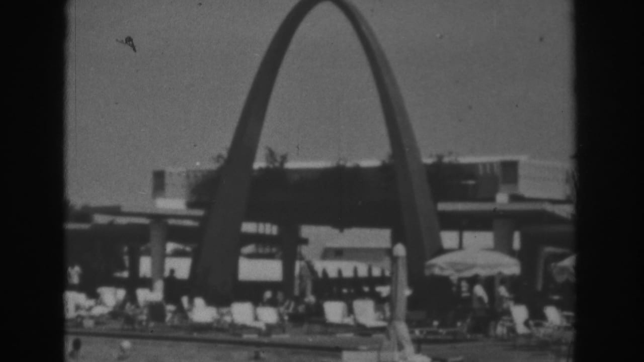 Poolside scene with a large arch, lounge chairs, umbrellas, and distant visitors.
