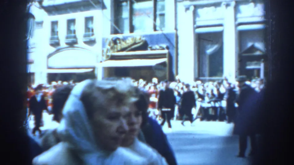 1962 New York City street parade view with a headscarfed woman close to camera and spectators beyond her.