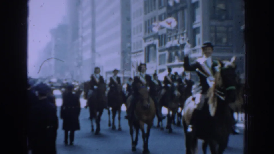 Mounted riders in formal clothing proceed along a New York City street during a 1962 parade, with buildings and spectators nearby.