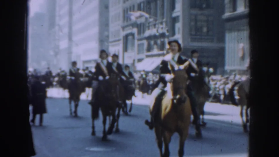 1962 New York City home-movie frame showing uniformed men on horseback in a parade with crowds along the street.