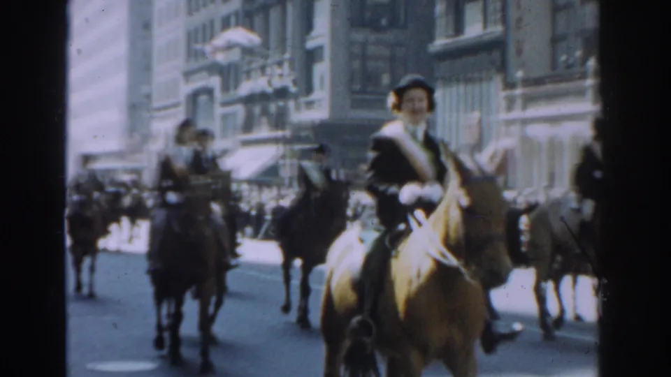 1962 New York City parade footage frame with a waving mounted rider, other horsemen, and spectators in the background.