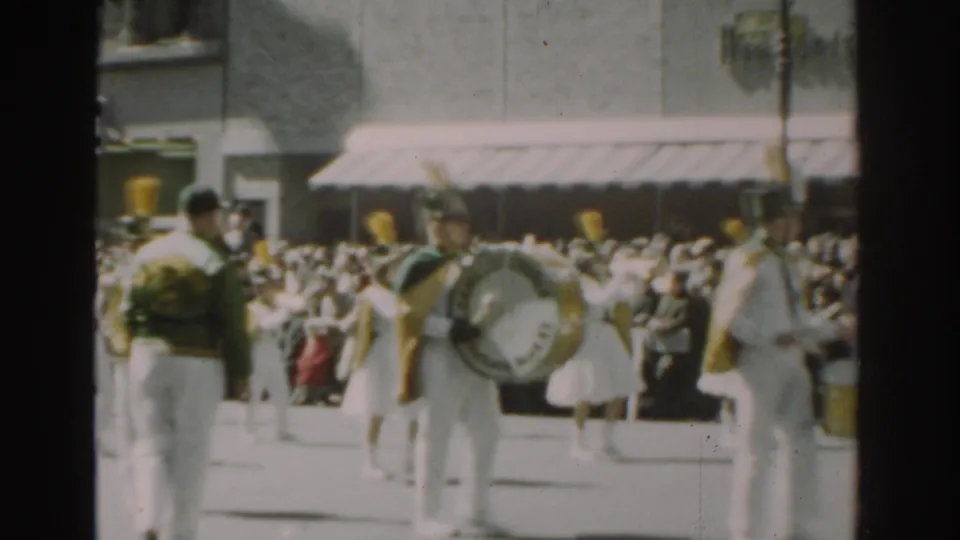 1962 New York City parade footage shows drummers in light uniforms marching past spectators along a sunlit street.