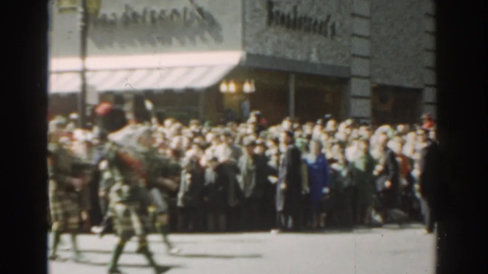 Bagpipers in tartan kilts march through a 1962 New York City parade while spectators watch from the sidewalk.